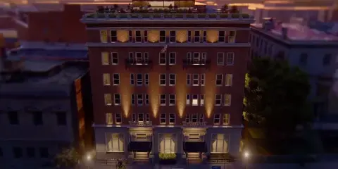 Exterior view of the Hotel Petersburg, a historic brick building with a rooftop terrace, at dusk.