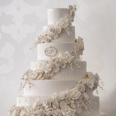 A five-tier white wedding cake decorated with cascading sugar roses and lace details.