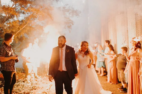 A bride and groom walking hand-in-hand through a tunnel of sparklers held by guests during a wedding celebration.