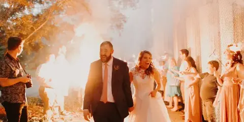 A bride and groom walking hand-in-hand through a tunnel of sparklers held by guests during a wedding celebration.