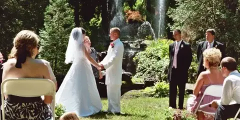A bride and groom exchanging vows during an outdoor wedding ceremony in a garden setting.