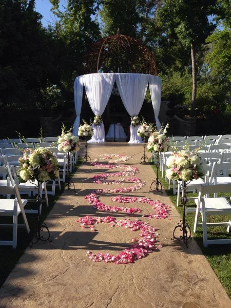 Outdoor wedding ceremony setup with a floral arch, white chairs, and a petal-lined aisle.
