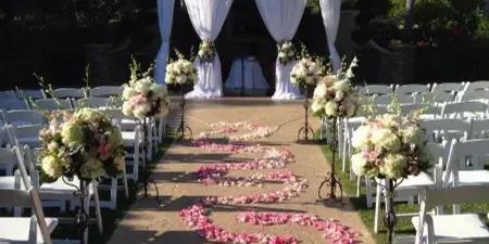 Outdoor wedding ceremony setup with a floral arch, white chairs, and a petal-lined aisle.