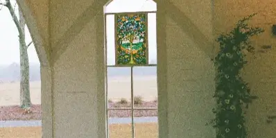 Interior view of a white chapel with a stained glass window, pews, and floral arrangements.