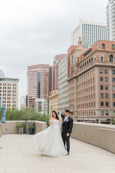 A bride and groom standing on a rooftop terrace with a city skyline in the background.