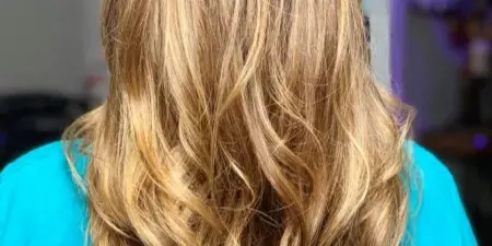 Back view of a client with long, wavy blonde hair showing a styled and colored finish.