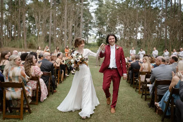 A bride and groom walking down the aisle at an outdoor wedding ceremony with guests seated on either side.