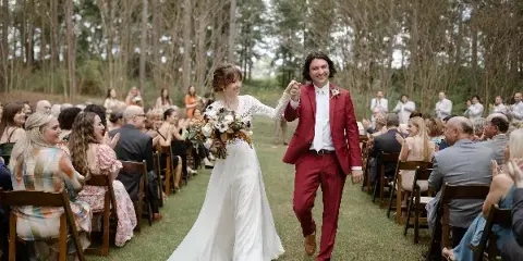 A bride and groom walking down the aisle at an outdoor wedding ceremony with guests seated on either side.