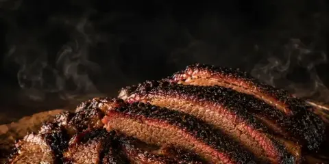 Sliced smoked brisket with a dark bark and visible smoke ring on a metal tray.