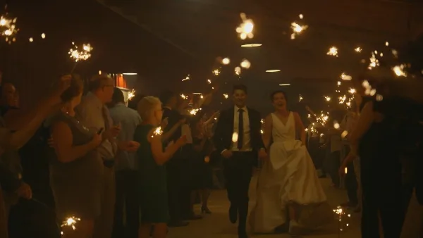 A bride and groom walking through a crowd of guests holding lit sparklers at a wedding reception.