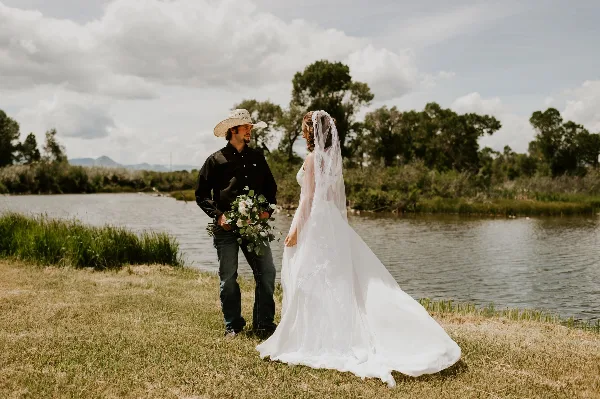 A bride and groom standing by a creek with a mountainous background.