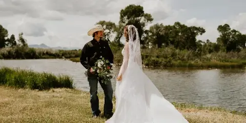 A bride and groom standing by a creek with a mountainous background.