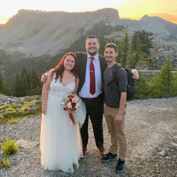 A bride and groom posing with a videographer on a mountain overlook at sunset