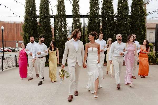 A bride and groom walking hand-in-hand with their wedding party in an outdoor setting.