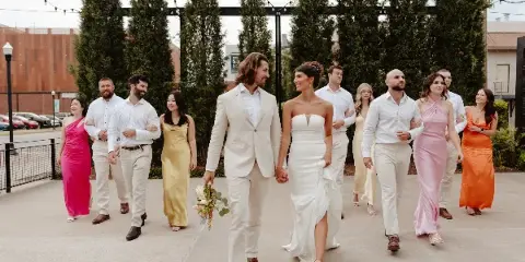 A bride and groom walking hand-in-hand with their wedding party in an outdoor setting.