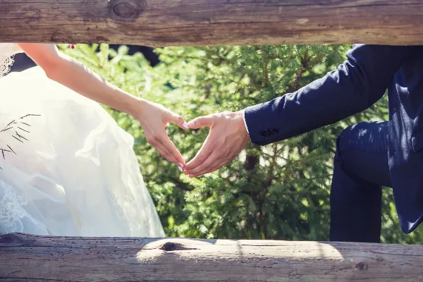 A bride and groom forming a heart shape with their hands outdoors.
