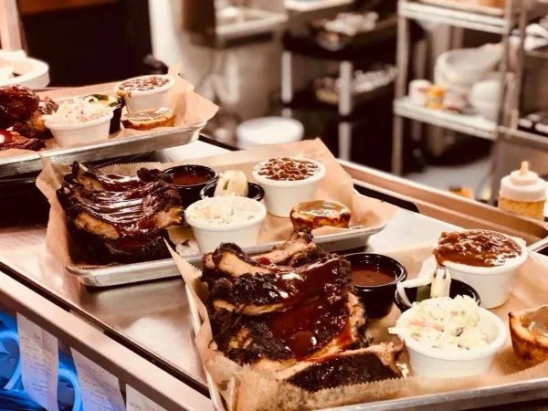 A catering table displaying trays of smoked ribs, brisket, and various side dishes.