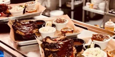 A catering table displaying trays of smoked ribs, brisket, and various side dishes.