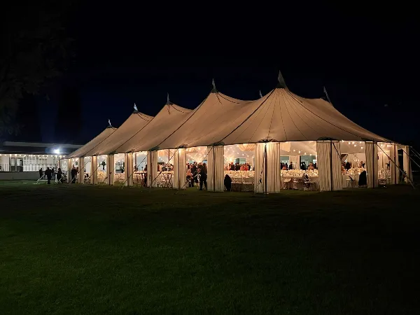 A large white event tent set up at night with tables and chairs visible inside.