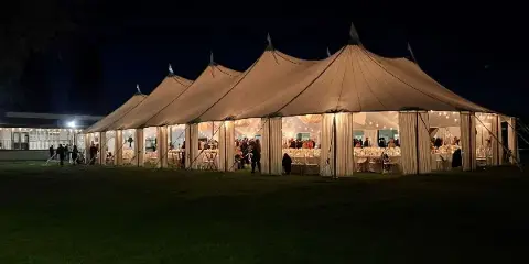 A large white event tent set up at night with tables and chairs visible inside.