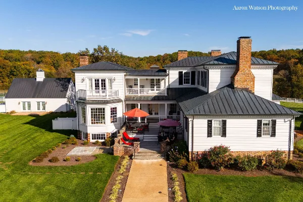 Aerial view of a large white wedding venue estate with a patio and green lawns.