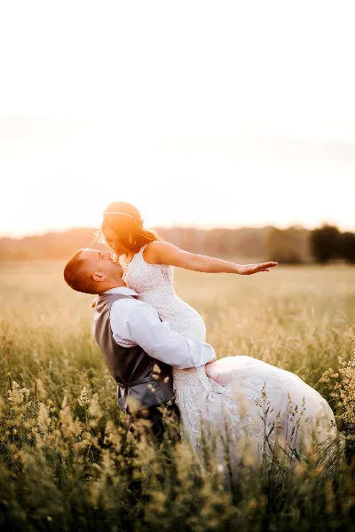 A bride and groom in a dip pose in a grassy field at sunset.