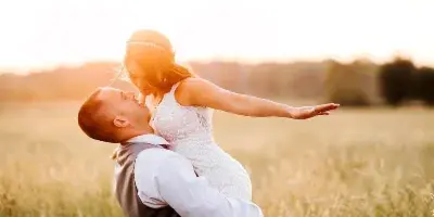 A bride and groom in a dip pose in a grassy field at sunset.