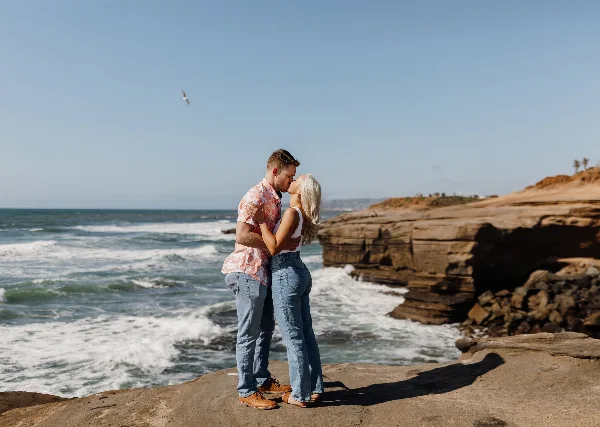 A couple kissing on a rocky cliff overlooking the ocean