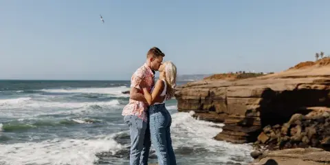 A couple kissing on a rocky cliff overlooking the ocean