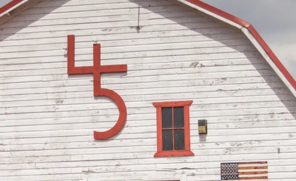 Exterior view of a white wooden barn with a large red number 45 sign and a small window.