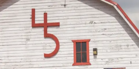 Exterior view of a white wooden barn with a large red number 45 sign and a small window.