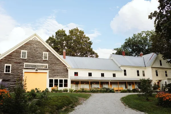 Exterior view of a rustic wooden barn with a yellow door and an adjacent white farmhouse building.