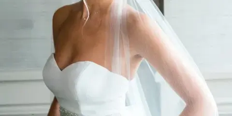 A professional portrait of a smiling bride in a white strapless gown and veil, holding a bouquet of flowers.