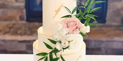 A three-tiered white wedding cake with fresh floral decorations and gold leaf accents on a table.