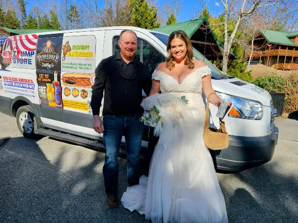 A bride and groom posing in front of a white passenger van.