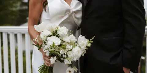 A bride in a white gown holding a white floral bouquet standing next to a groom in a black suit.