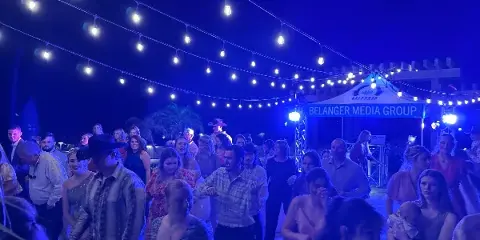 Outdoor wedding reception at night with guests dancing under string lights near a DJ booth labeled Belanger Media Group.