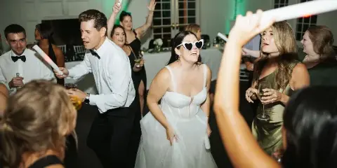 A bride and wedding guests dancing at a reception with glow sticks and green uplighting.