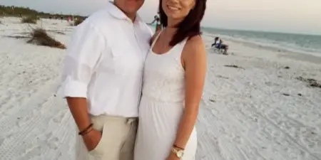 A couple in white wedding attire standing on a sandy beach.