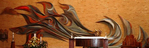 Interior view of a church sanctuary featuring a wooden altar and a large, colorful abstract mural on a brick wall.