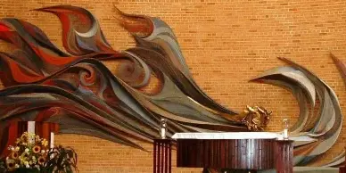 Interior view of a church sanctuary featuring a wooden altar and a large, colorful abstract mural on a brick wall.