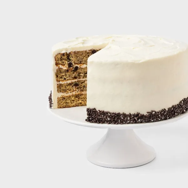 A multi-layered cake with white frosting and chocolate sprinkles on a white cake stand