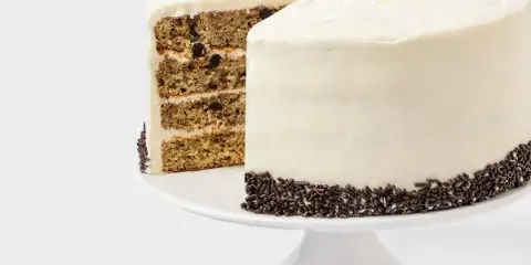 A multi-layered cake with white frosting and chocolate sprinkles on a white cake stand