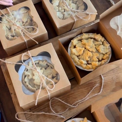 Rustic cardboard boxes containing pies and cookies, tied with twine, arranged on a wooden table.