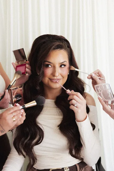 A professional makeup artist applying makeup to a smiling client using brushes and cosmetics.