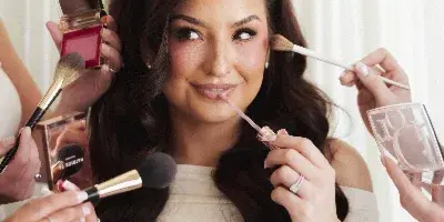 A professional makeup artist applying makeup to a smiling client using brushes and cosmetics.