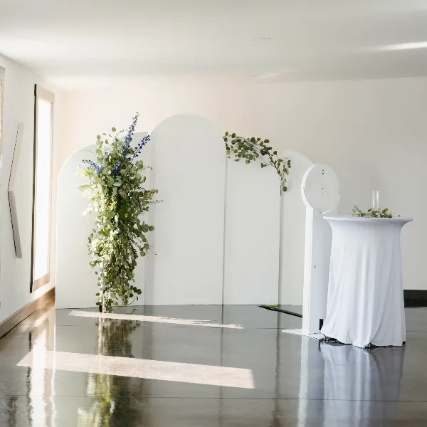 White arched backdrops with greenery and a draped table set up for an event