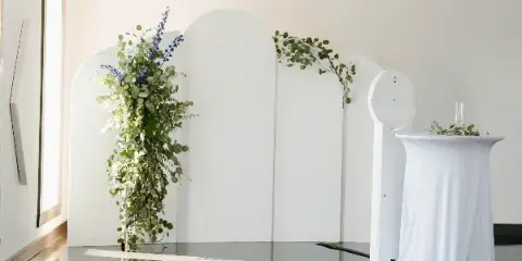 White arched backdrops with greenery and a draped table set up for an event