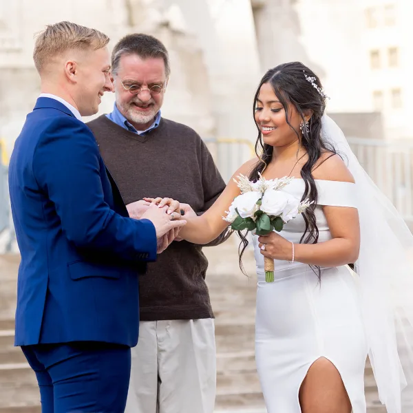 A wedding officiant placing a ring on a bride's finger during a ceremony.