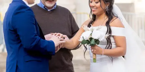 A wedding officiant placing a ring on a bride's finger during a ceremony.
